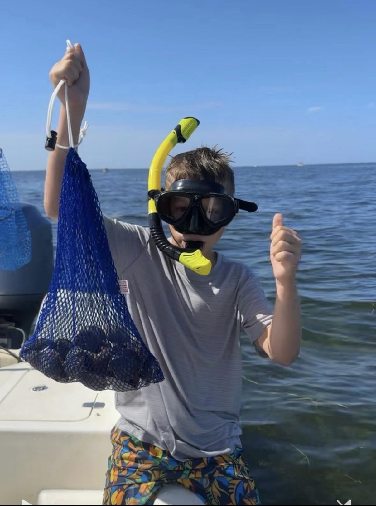 Young snorkeler giving a thumbs up with a mesh bag full of fresh Crystal River bay scallops.